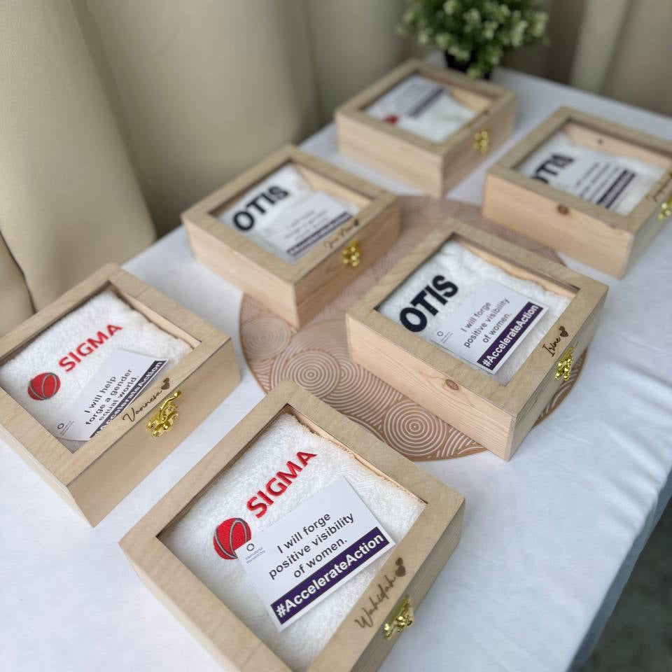 Corporate gift set with face towels and wooden boxes, embroidered with logos, displayed on tables with curtains in the background.