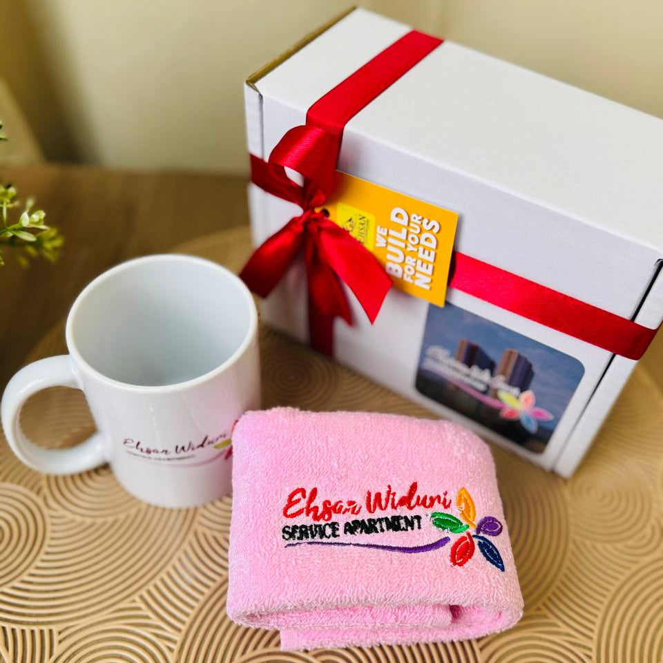 Corporate gift ser Pink towel with branding, white mug, and gift box with red ribbon on a wooden surface